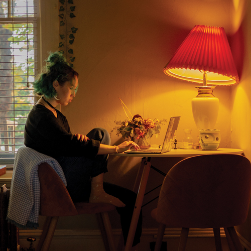 A student sits at home at a corner desk using a laptop