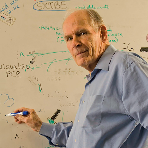 Ben Hall stands at a whiteboard holding a blue marker and wearing a light blue shirt.