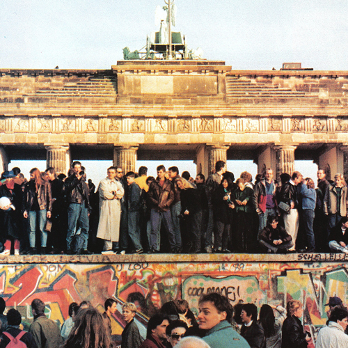 A large crowd stands near and on top of the Berlin wall