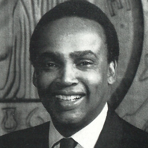 Headshot of Norm Rice from the chest up wearing a black suit and tie