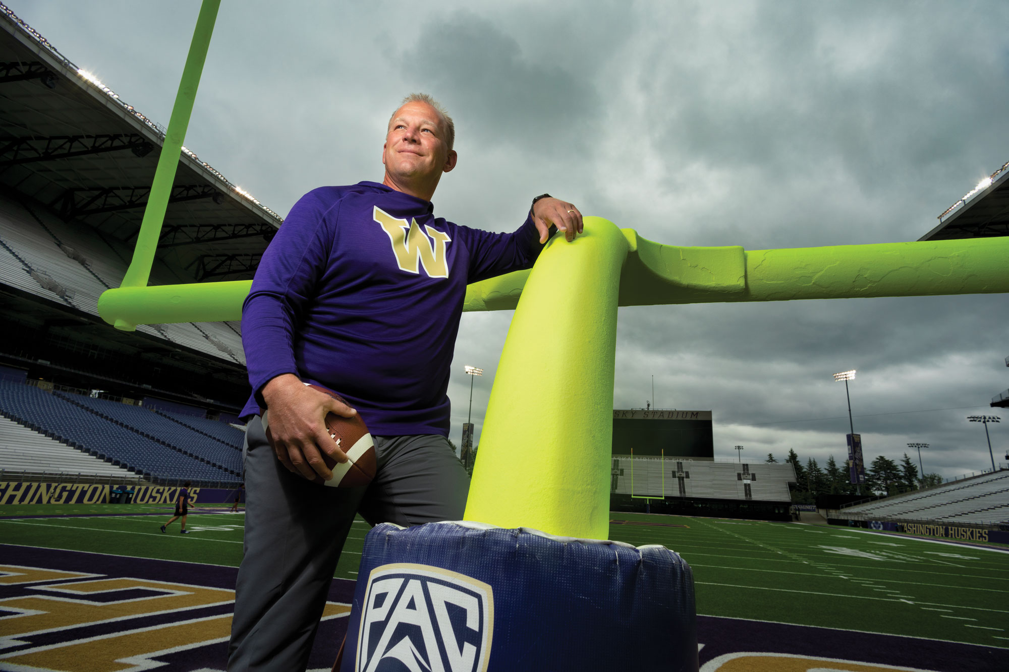 Football coach Kalen DeBoer leans against a goal post holding a football