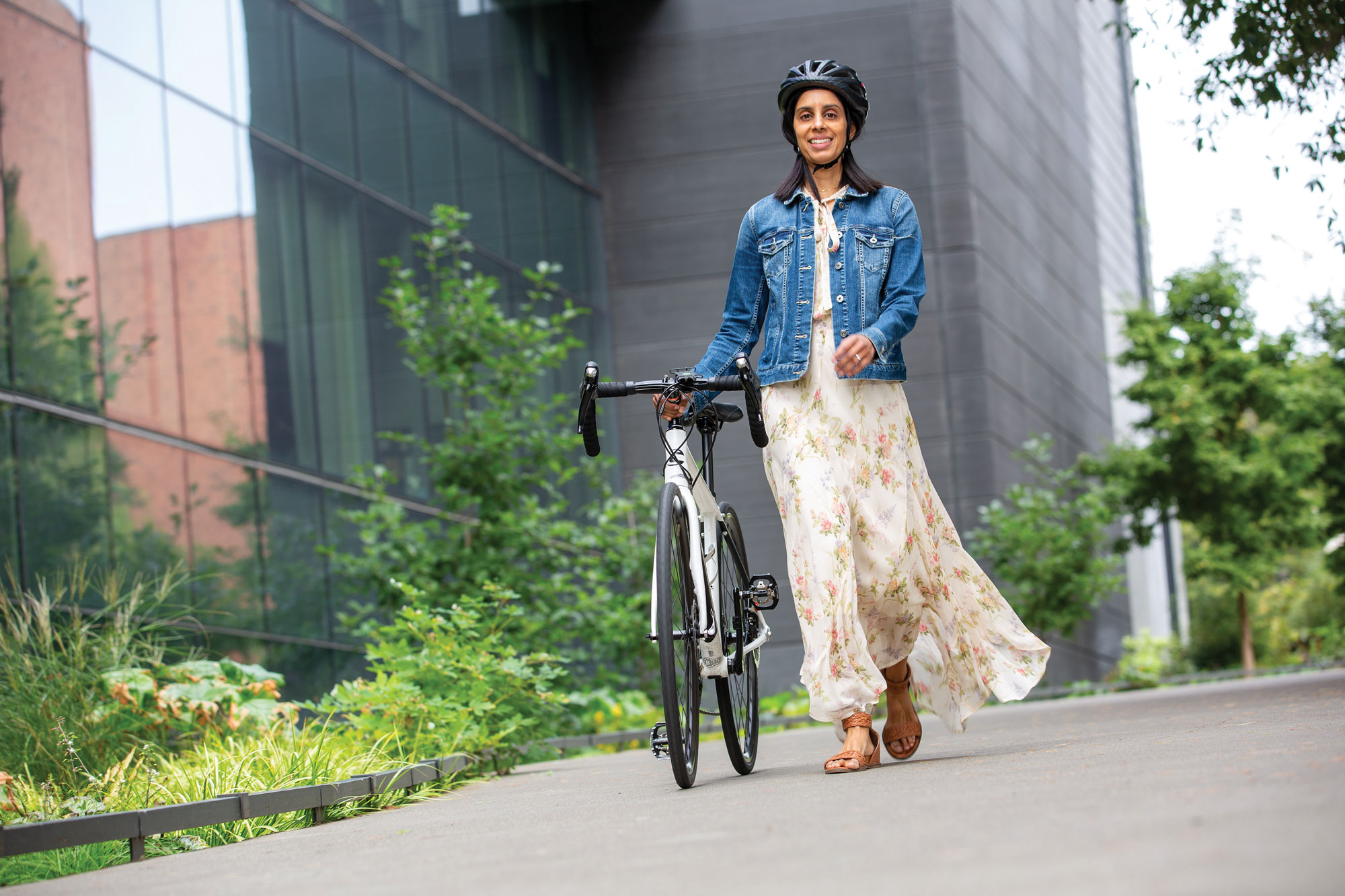 A woman in a long flowy dress walks alongside her bike.