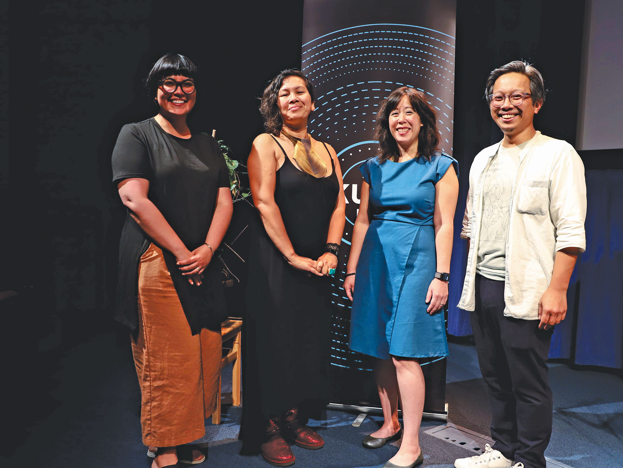 Four people stand on a stage, posed and smiling