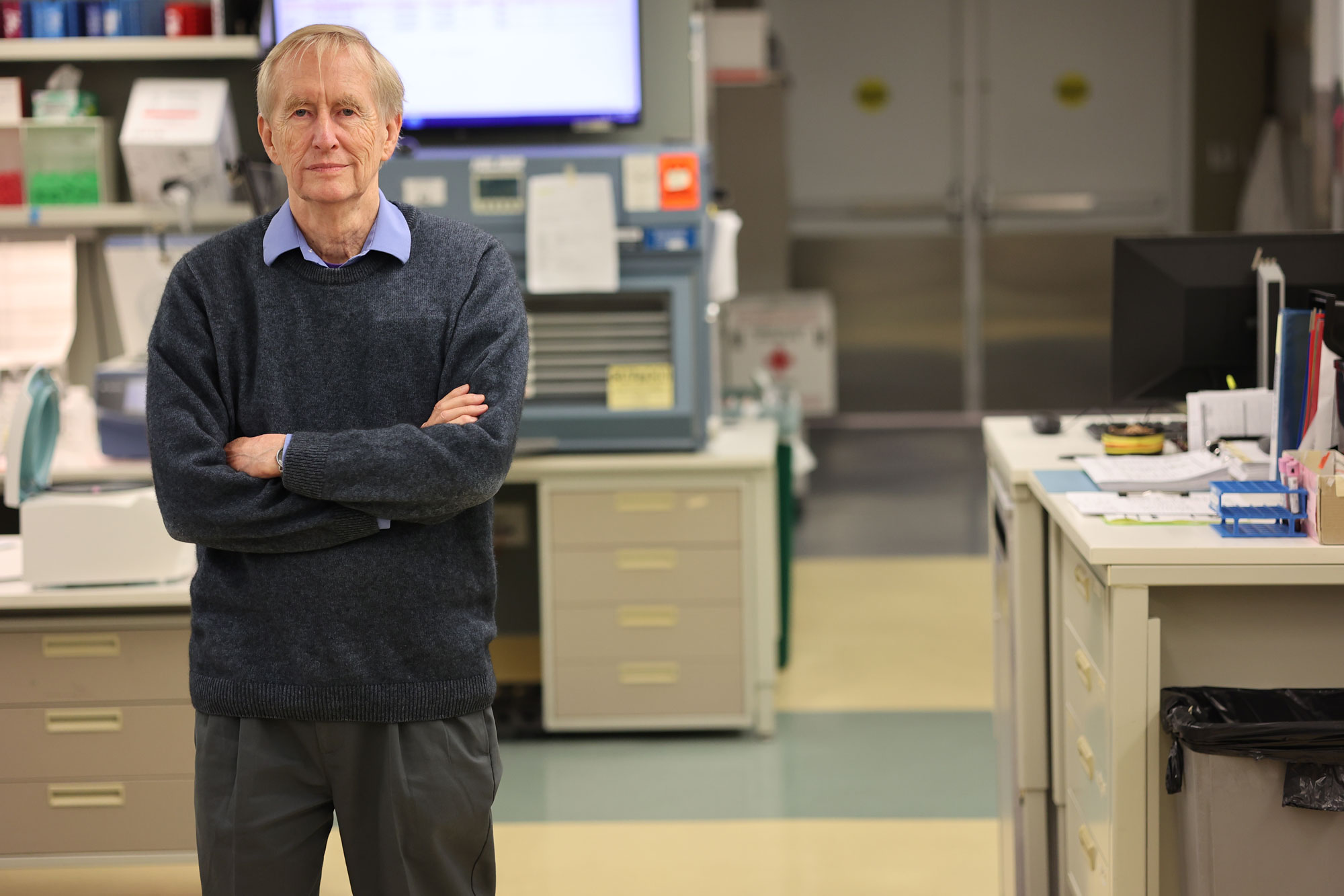 A man in business casual clothing stands cross-armed in a laboratory.