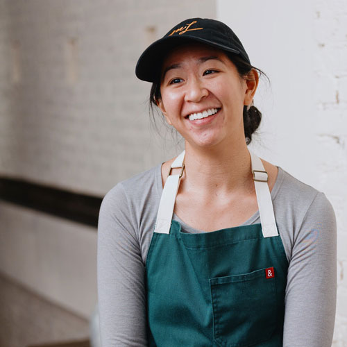 A woman in a green apron smiles at a customer