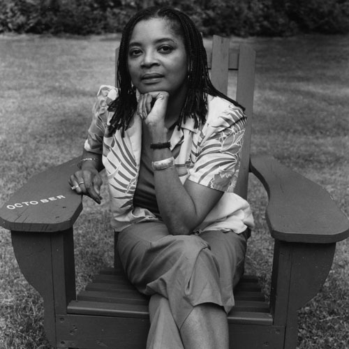 A Black woman sits in an Adirondack chair with her chin resting on a fist.