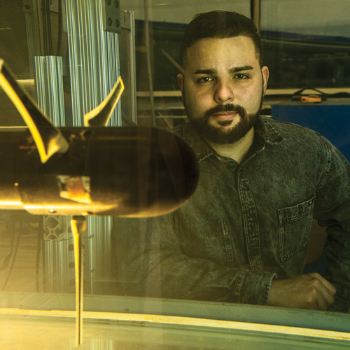 A man with a beard stares with determination in front of laboratory equipment