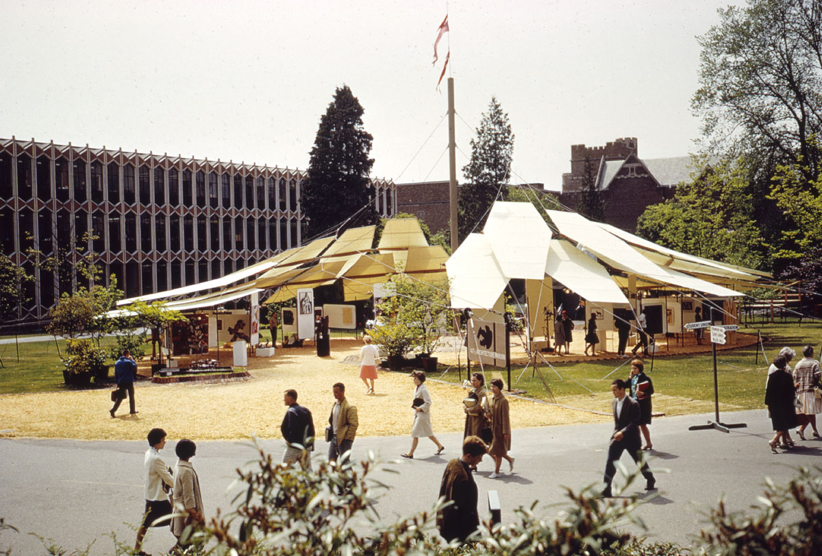 A color film photo of an art installation featuring large shades over the Hub Lawn. Students in business casual 1950s attire walk nearby.