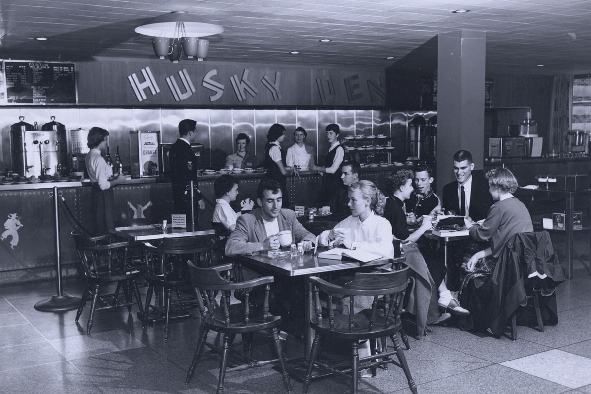 A film photo of students at dining tables in the 1950s inside the HUB dining room, called the Husky Den