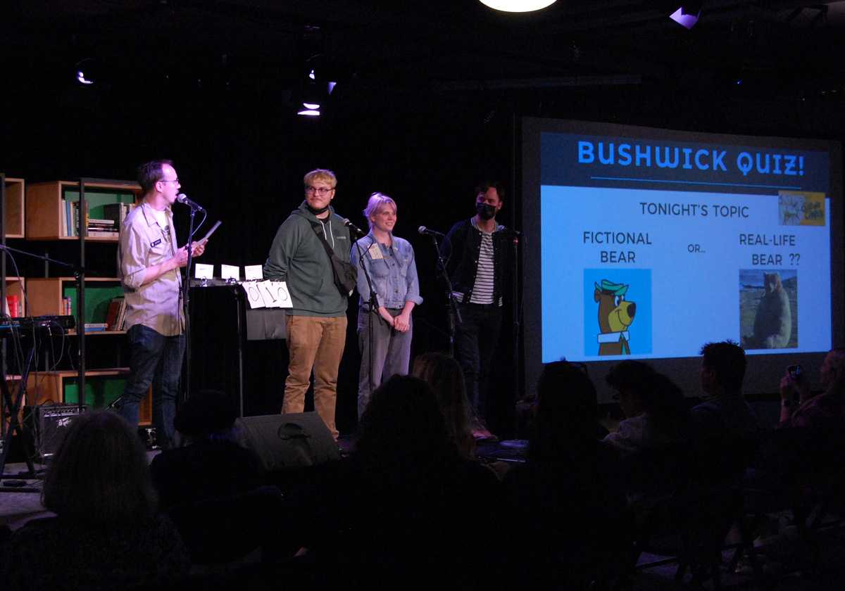 Several people stand in front of microphones onstage in front of an audience