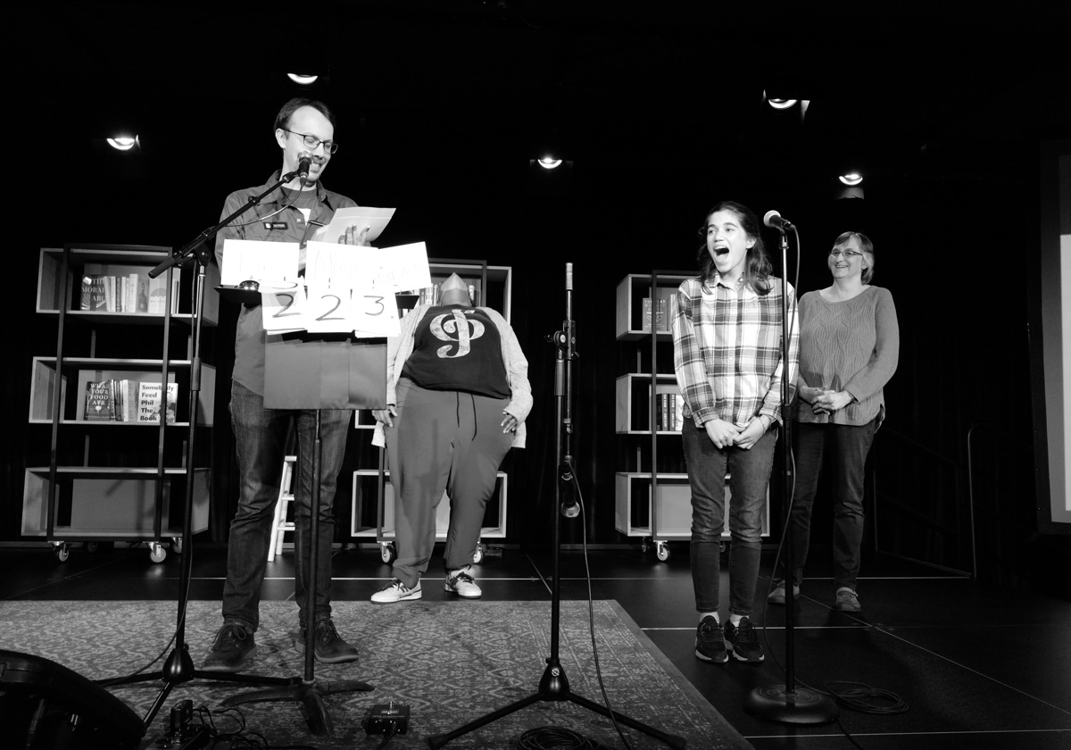 A woman onstage looks surprised as Wes Weddell reads from a piece of paper