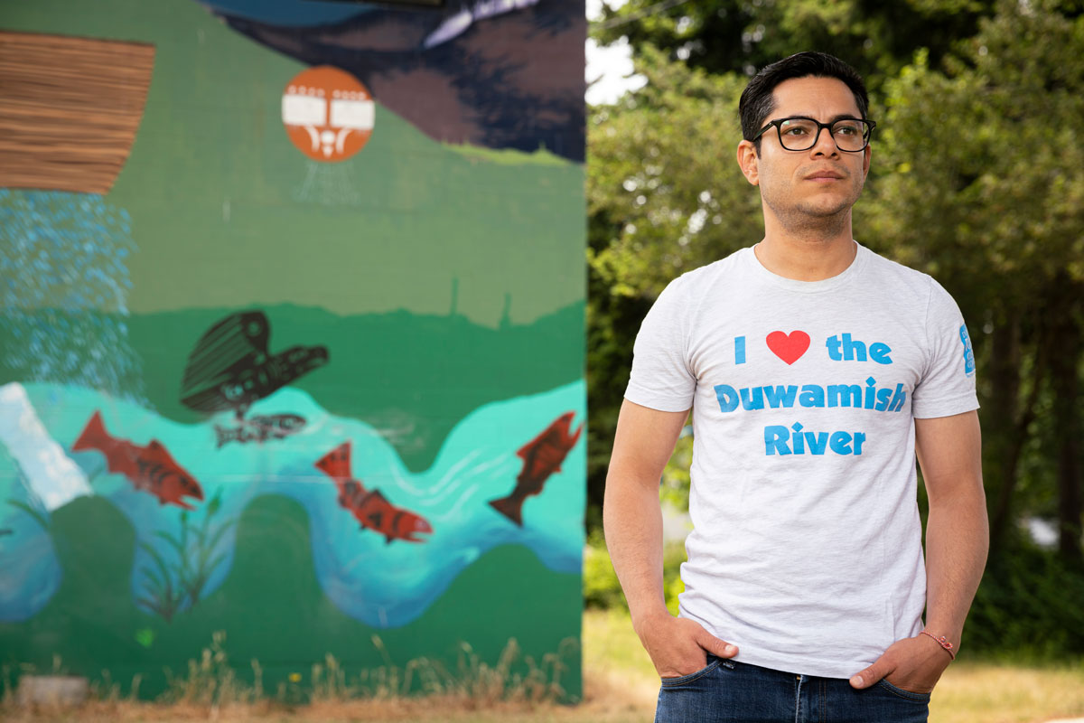 A man stands near a mural featuring fish in a river.