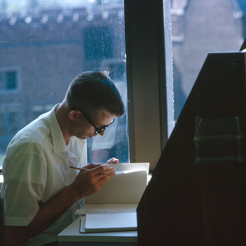 An old photo of a college student flipping through papers in a library