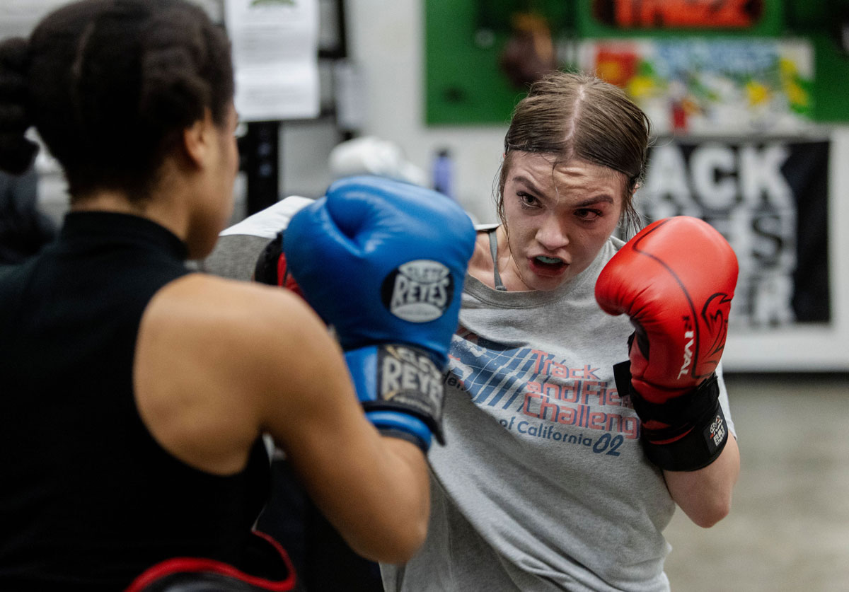 Two women box, wearing red and blue gloves