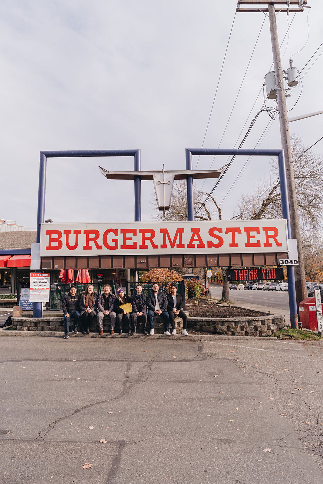 A group of people sits in front of the Burgermaster sign in the U District