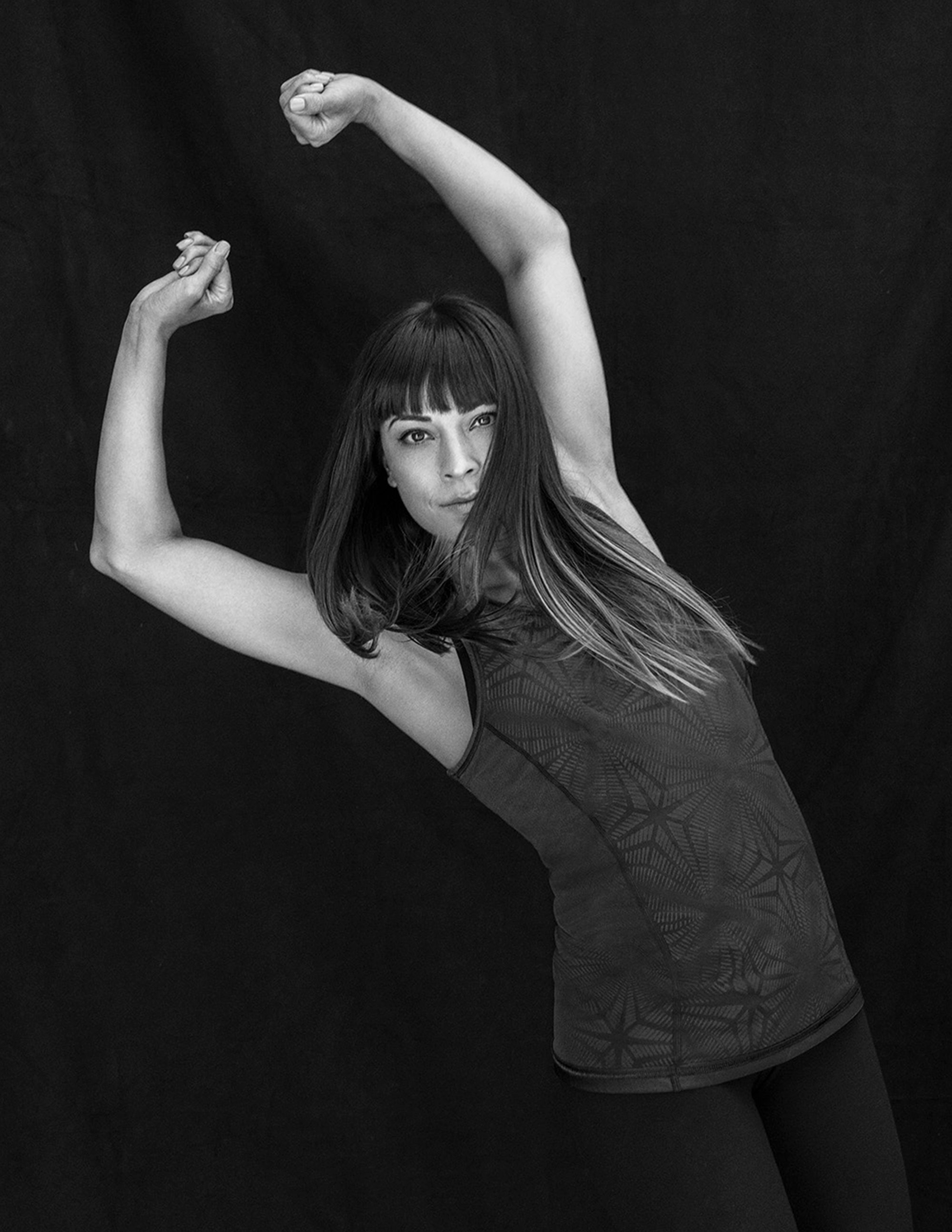 Black and white studio portrait of a woman dancing with her arms in the air