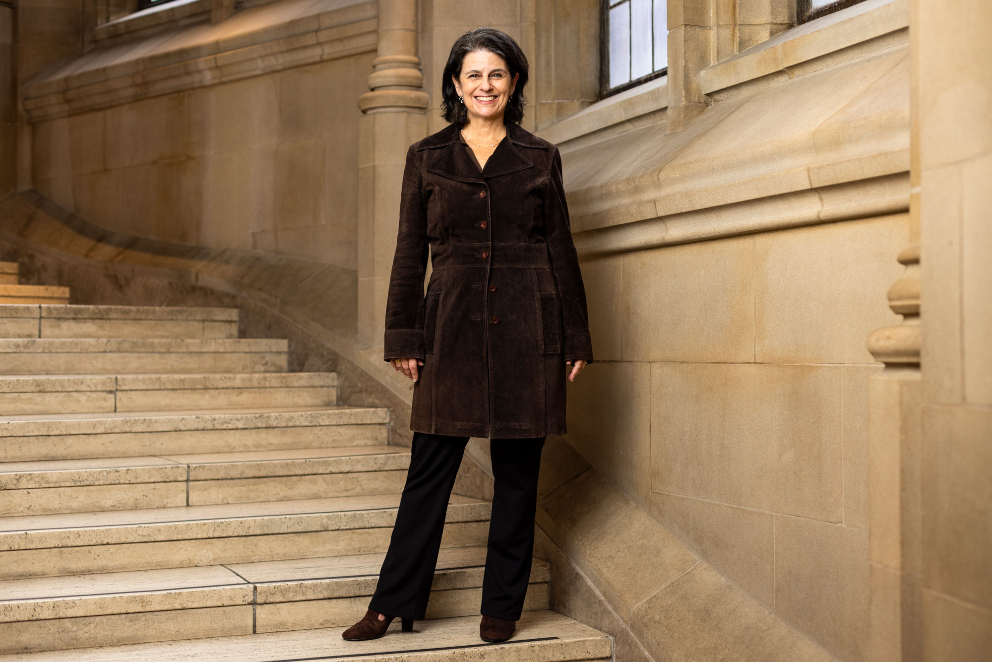 A woman in a brown corduroy jacket smiles on the steps of Suzzallo Library