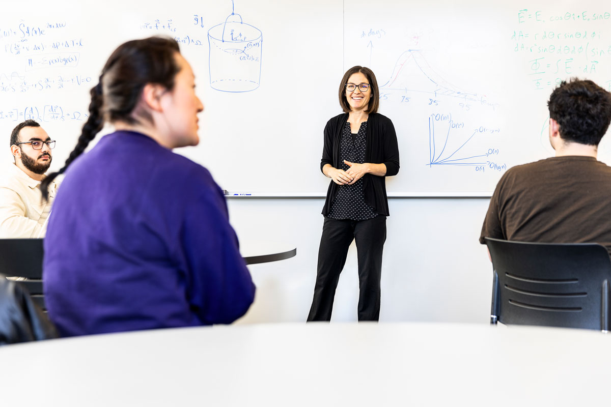 Professor Joey Kay smiles as her students have a discussion in a classroom.