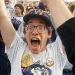 A man cheers and raises his arms at a sporting event