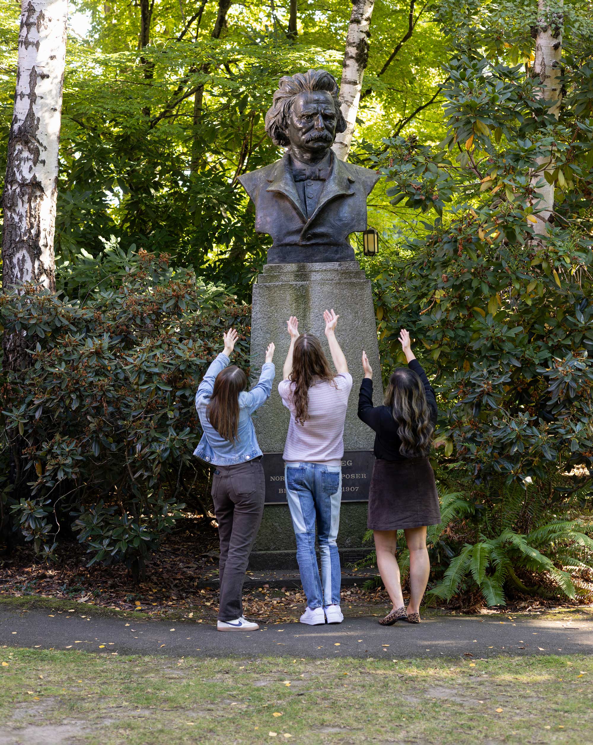Three people gesturing to a statue of Edvard Grieg without a shiny nose