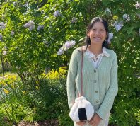 A woman wears a homemade bag in front of a flower bush