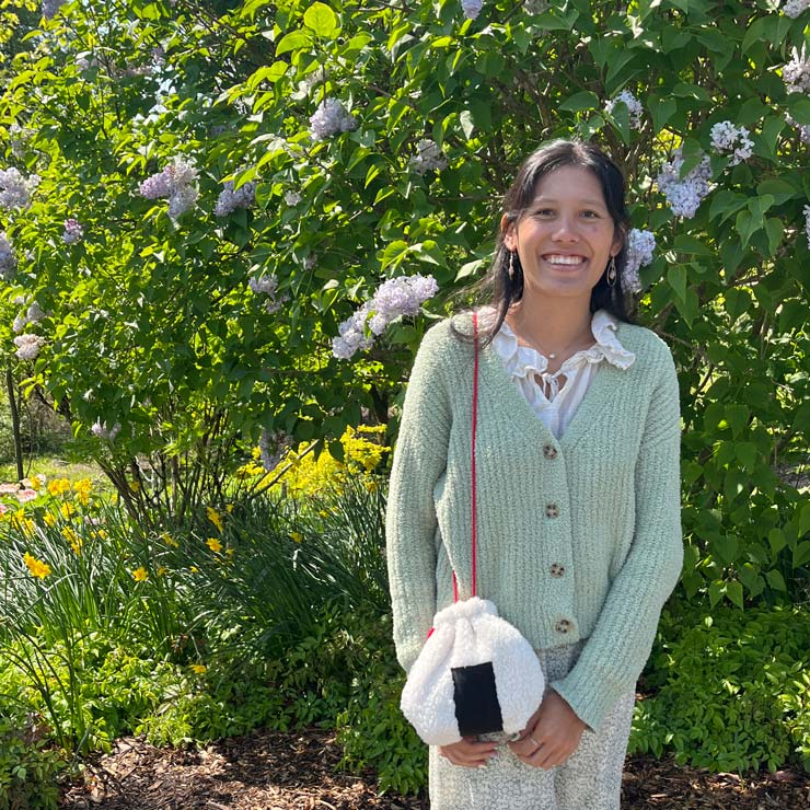 A woman wears a homemade bag in front of a flower bush