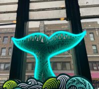 A neon-lit whale tail sculpture sits in the window of Tai Tung
