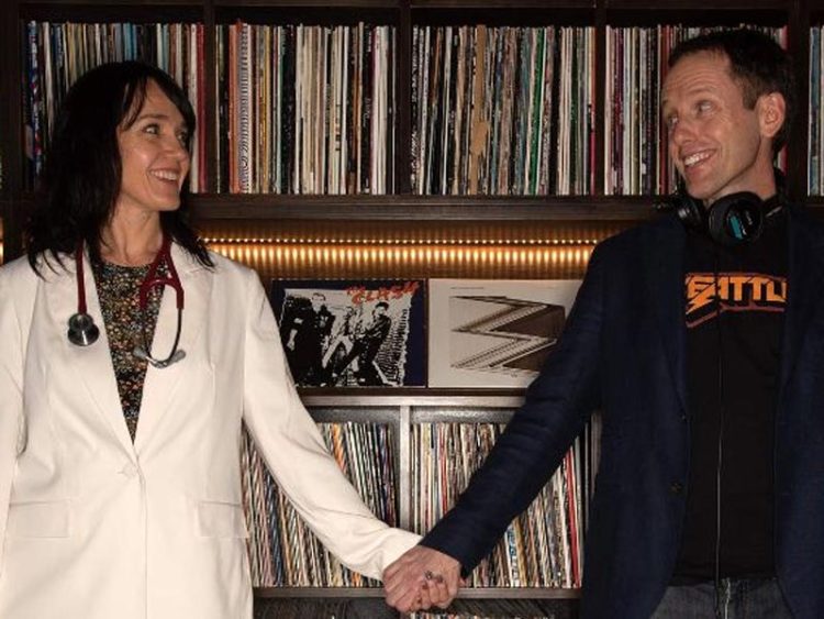 A doctor and her DJ husband holding hands in front of a record shelf