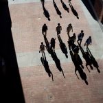Students walk through campus. Their shadows are long in front of them.
